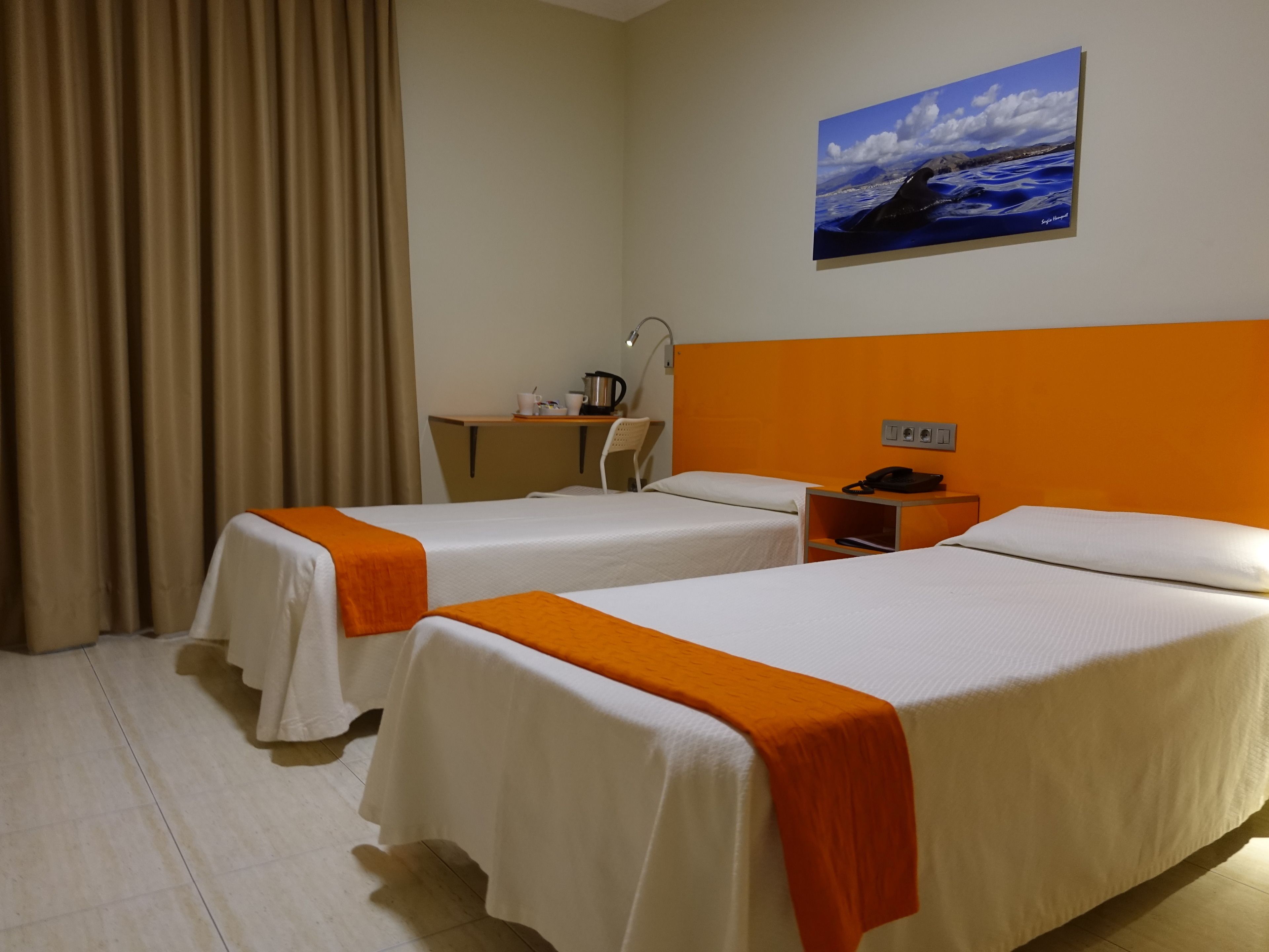 Une chambre d’hôtel avec deux lits, un bureau, une chaise, un tableau et un rideau.