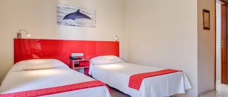 Habitación de hotel con dos camas, un cabecero rojo, un cuadro de delfín y un escritorio pequeño con una lámpara.