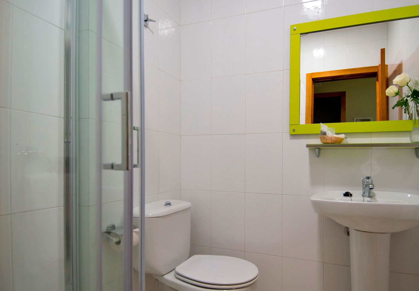 Un baño con cabina de ducha de vidrio, inodoro blanco y lavabo con espejo superior.