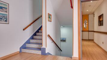A staircase with blue patterned steps leading to a hallway with wooden flooring and a door with a red sign.