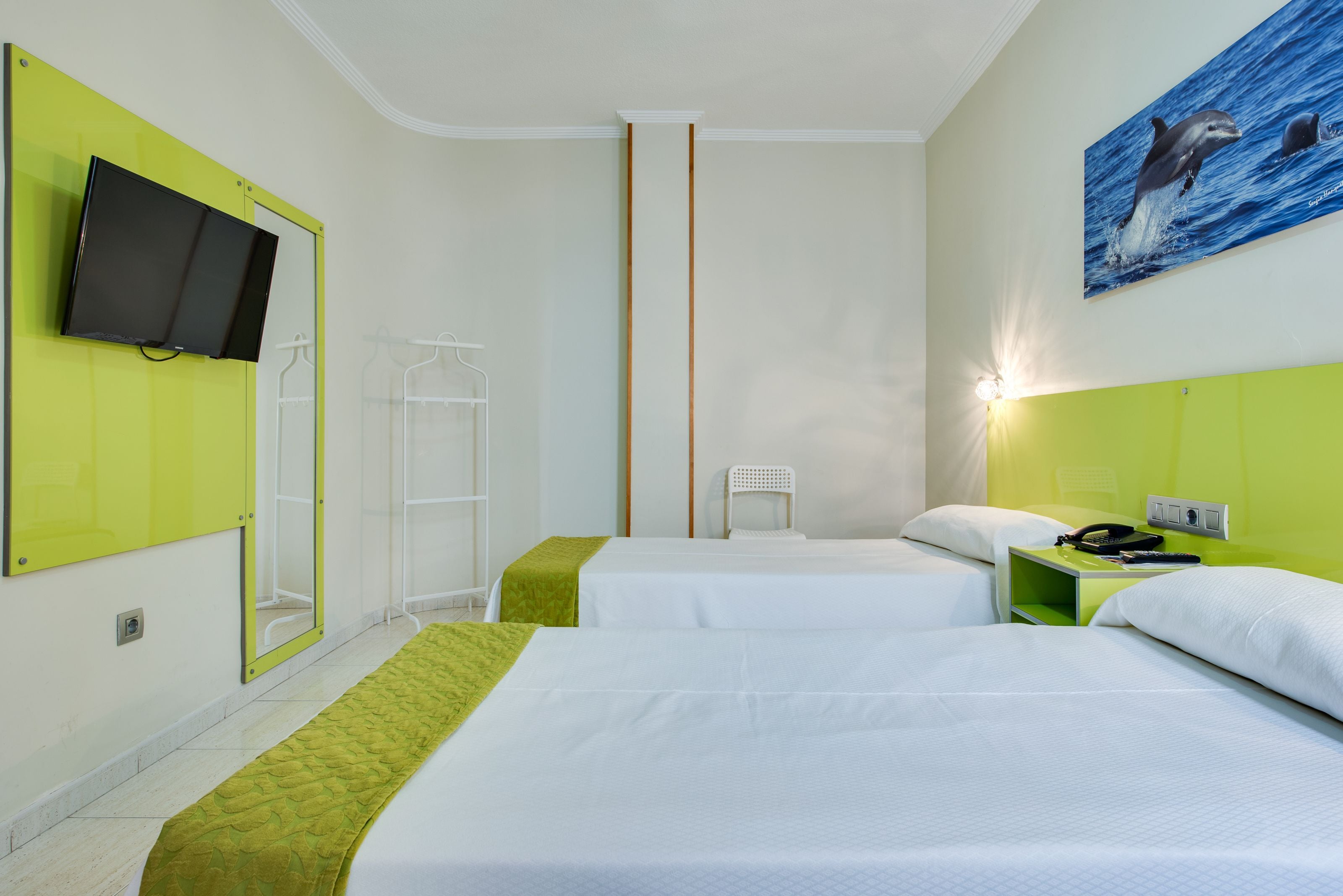 Habitación de hotel con dos camas, un televisor montado en la pared, un cuadro de delfín y una pared de acento verde.