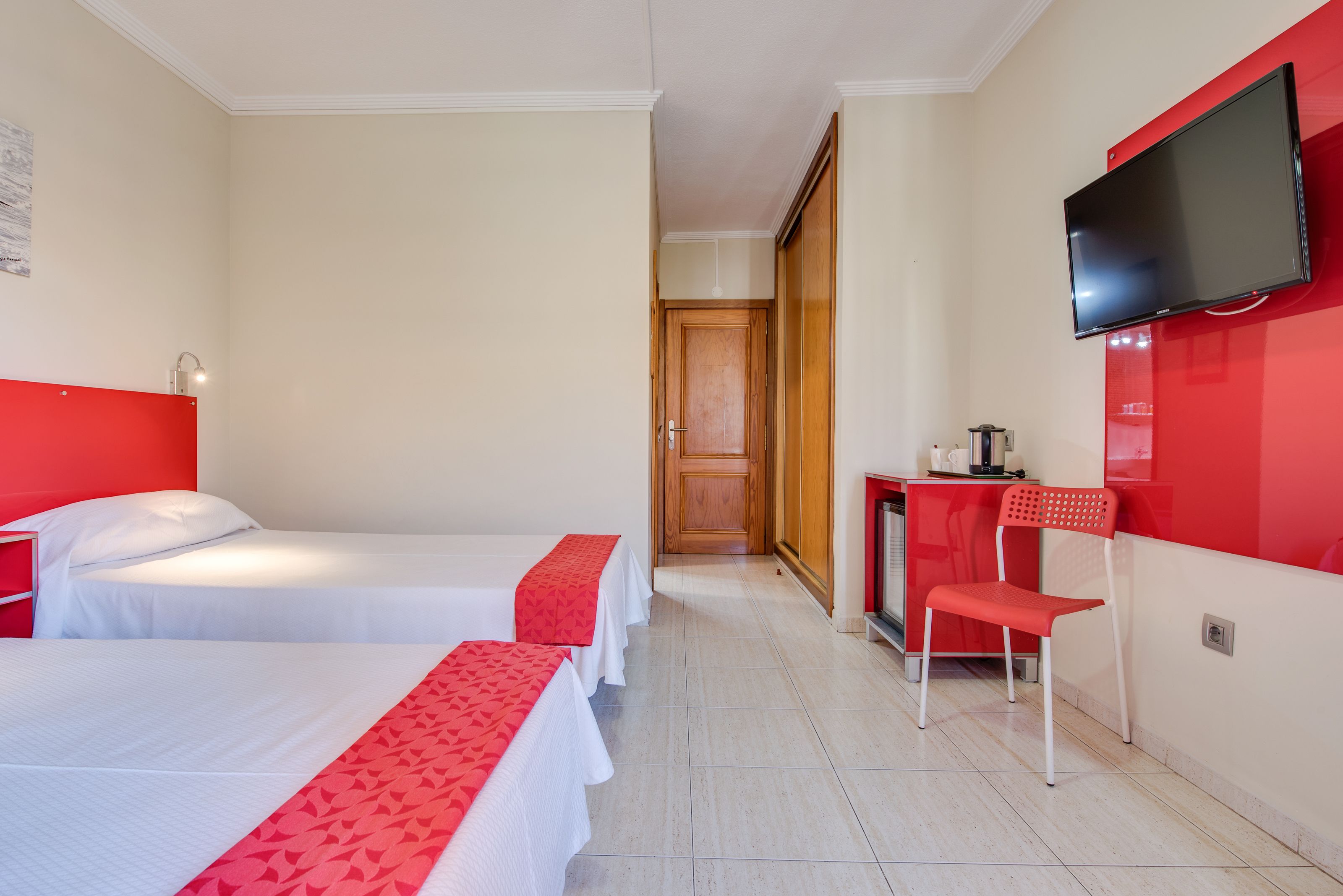A hotel room with two beds, a desk, a chair, and a TV.