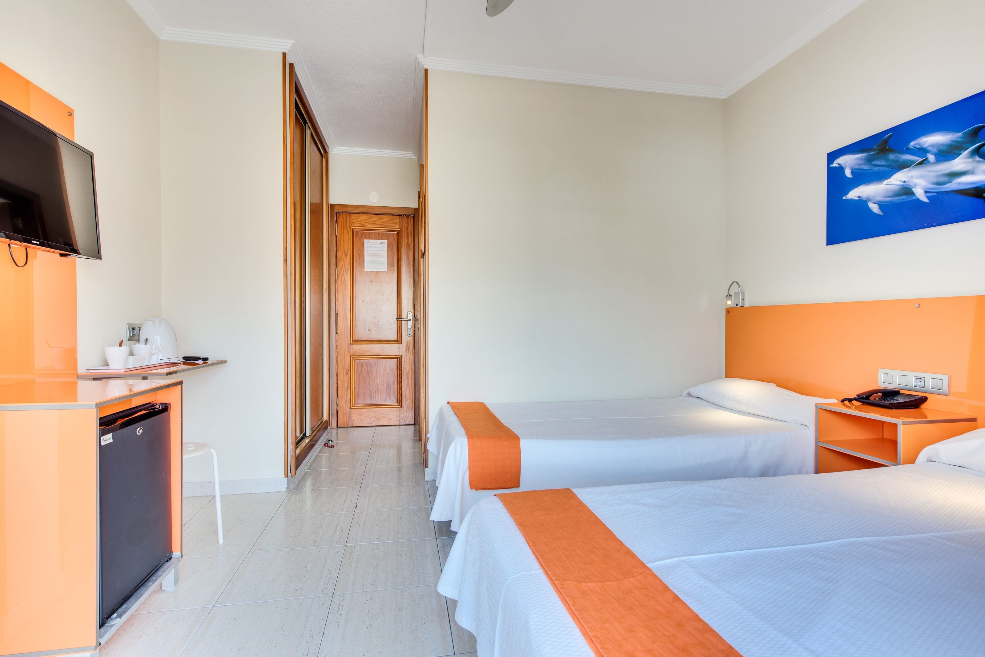 A hotel room with two beds, a TV, a desk with a coffee machine, and a bathroom visible through an open door.