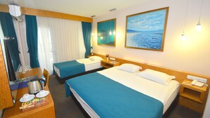 Hotelkamer met twee bedden, een bureau met een waterkoker, een spiegel en een schilderij van een strand.