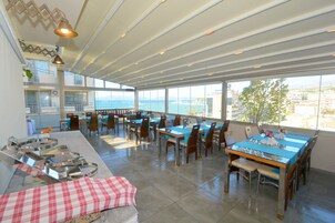 Un comedor amplio con varias mesas y sillas, ventanas grandes que ofrecen vistas al mar, y un diseño moderno de techo.