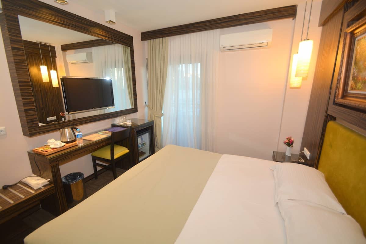 Une chambre d’hôtel avec un grand lit, un bureau avec une chaise, une télévision et un miroir.