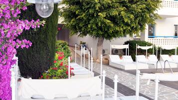 Une terrasse sur le toit avec des chaises longues blanches, un pot de fleurs et un grand arbre.