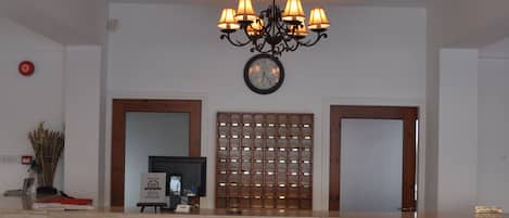 A lobby with a wooden ceiling, a chandelier, a clock, and a reception desk.
