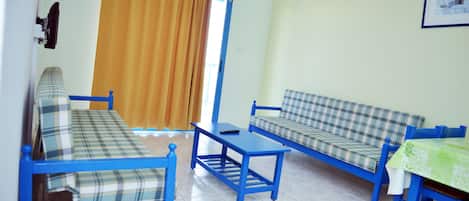 A room with two blue sofas, a small table, and a window with orange curtains.