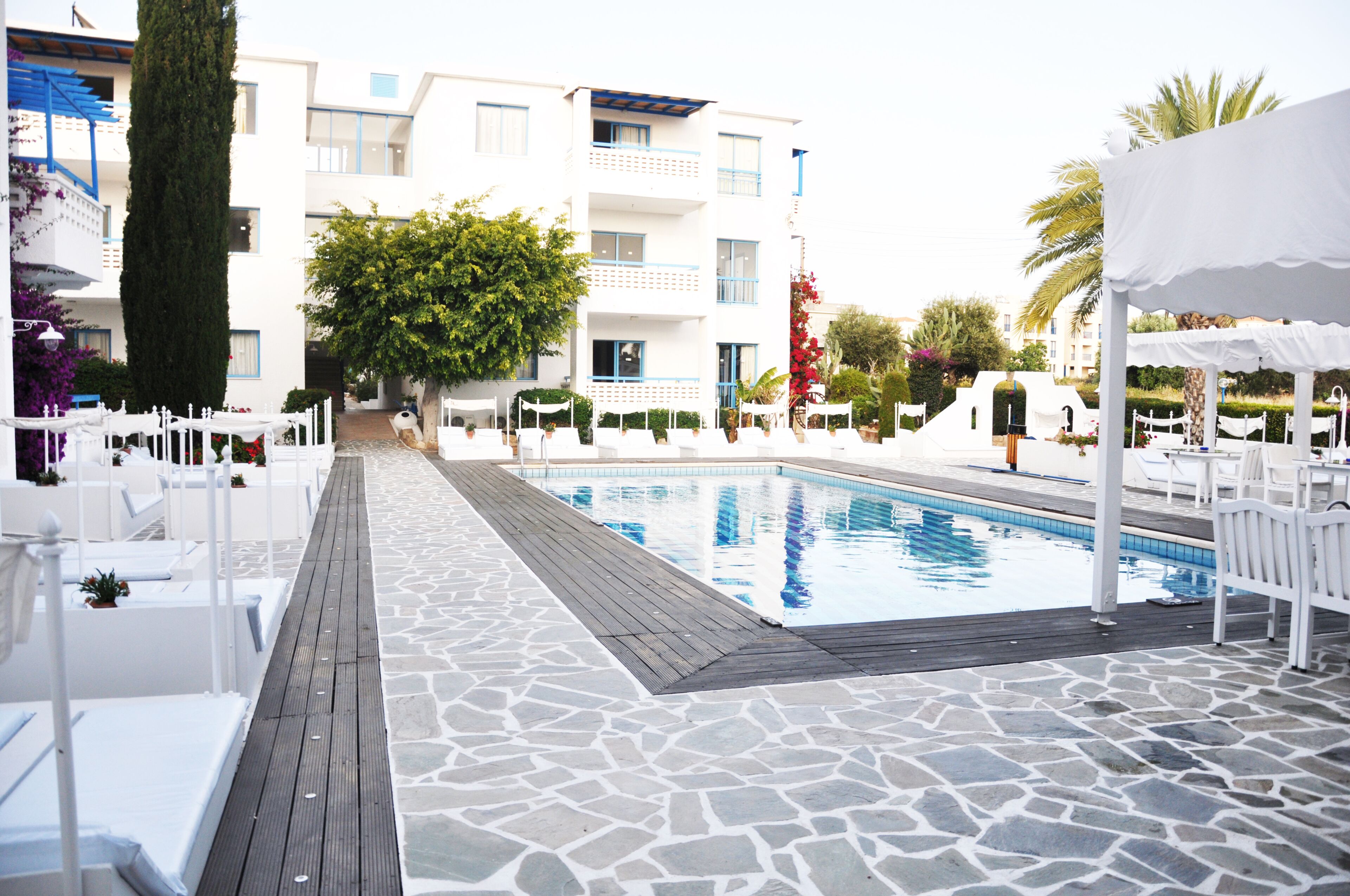 A poolside area with a stone-tiled deck, white lounge chairs, and a clear blue pool.