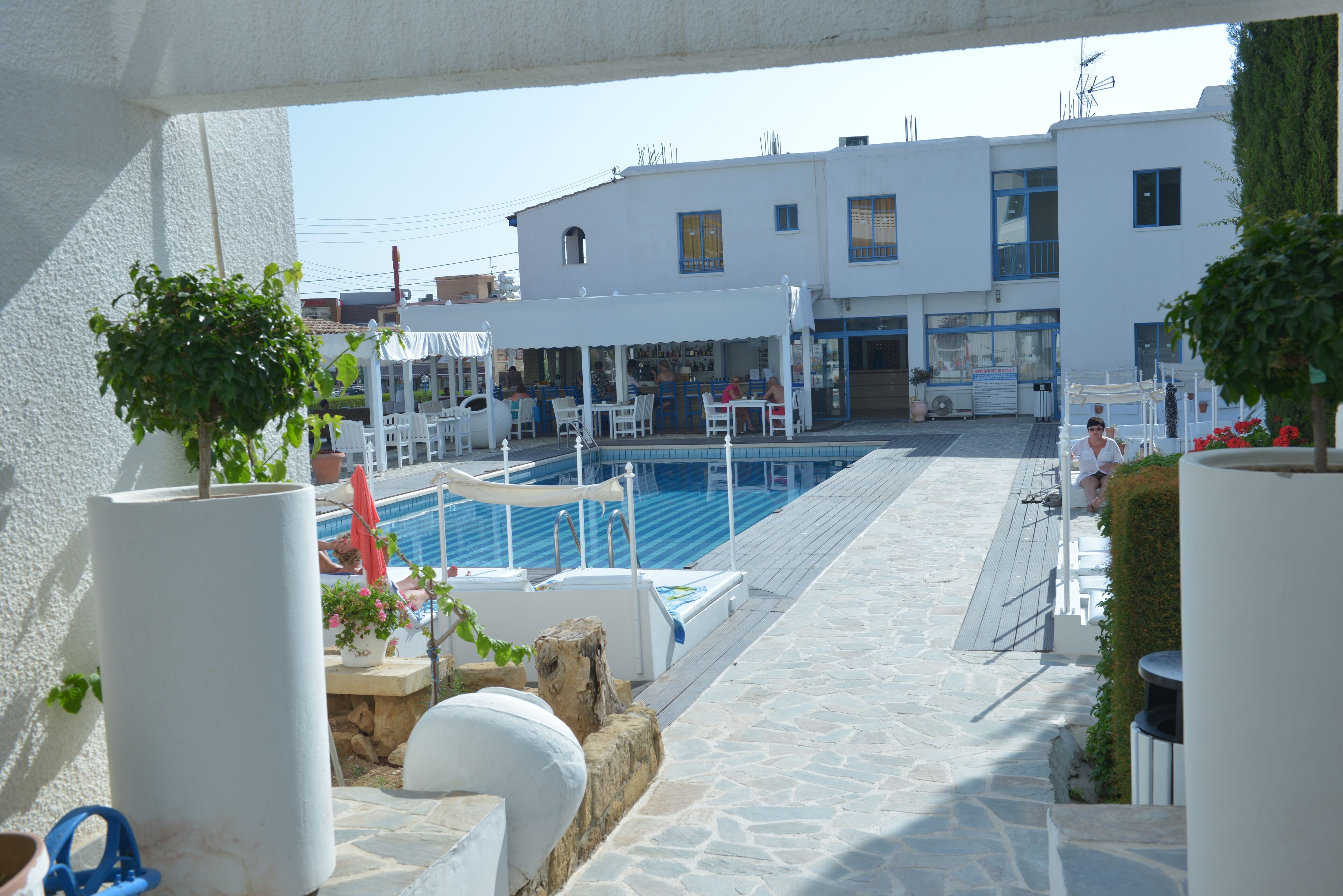 Un espace aménagé au bord de la piscine, avec une terrasse en pierre, des bâtiments blancs en arrière-plan et des plantes en pot.