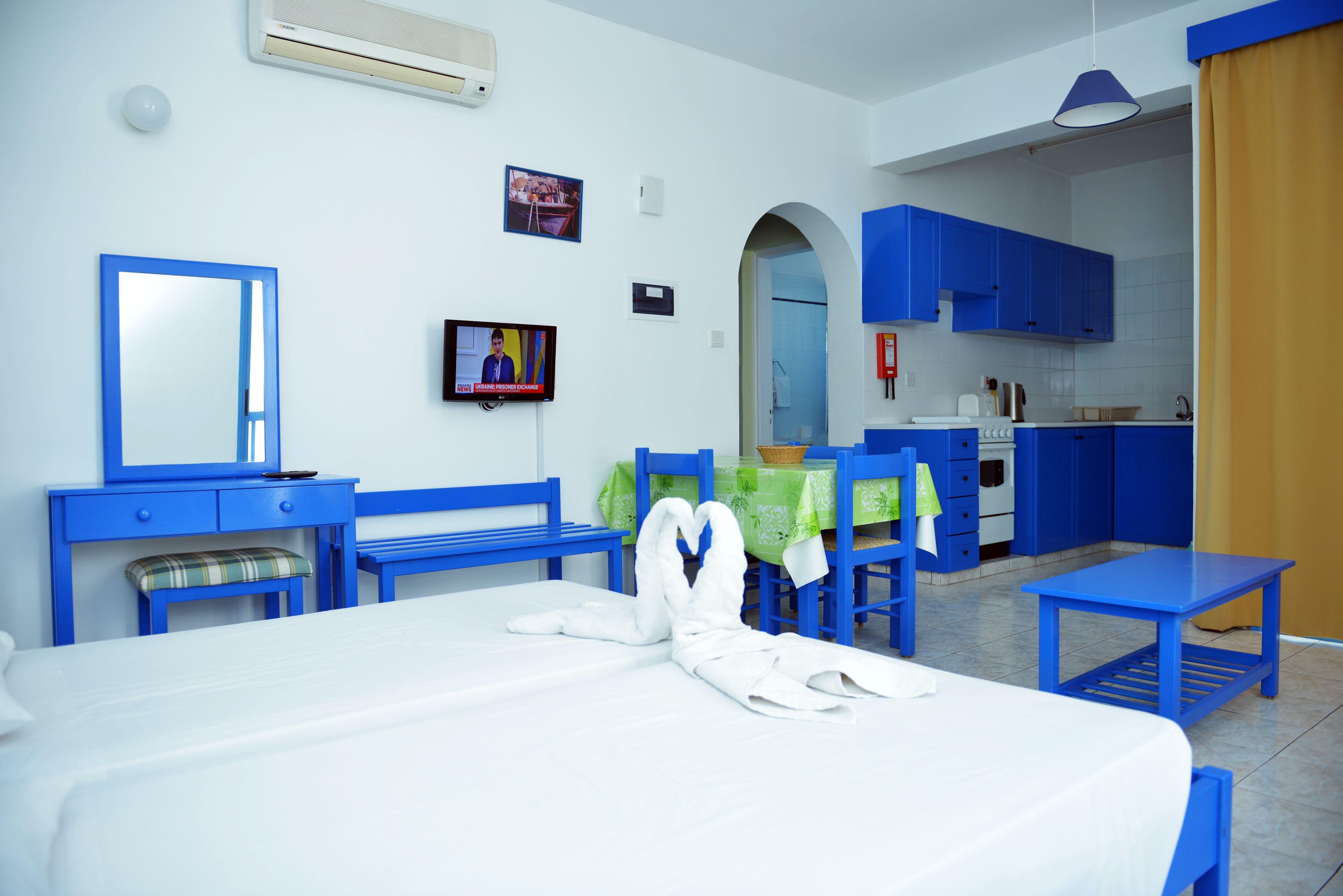 Een hotelkamer met een bed, een bureau, een stoel, een televisietoestel en een kitchenette.