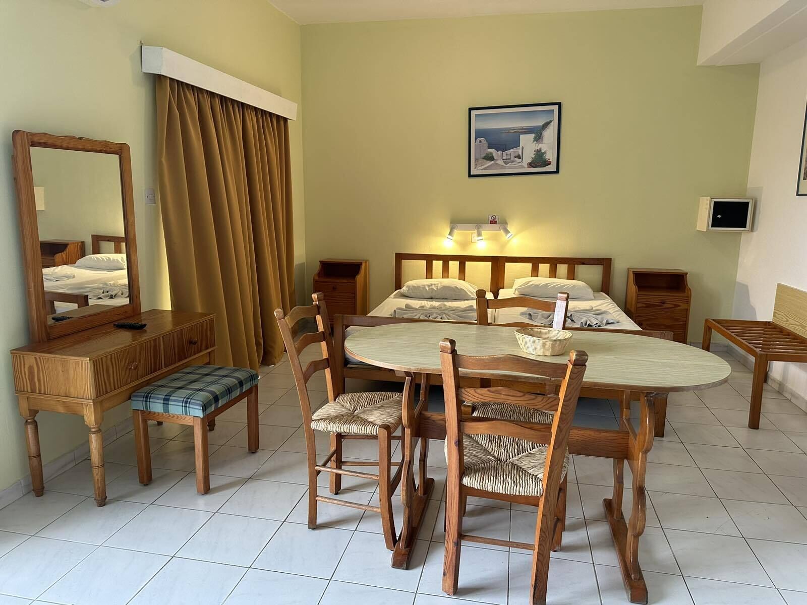 Een hotelkamer met een bed, een eettafel met stoelen, een spiegel en een schilderij aan de muur.