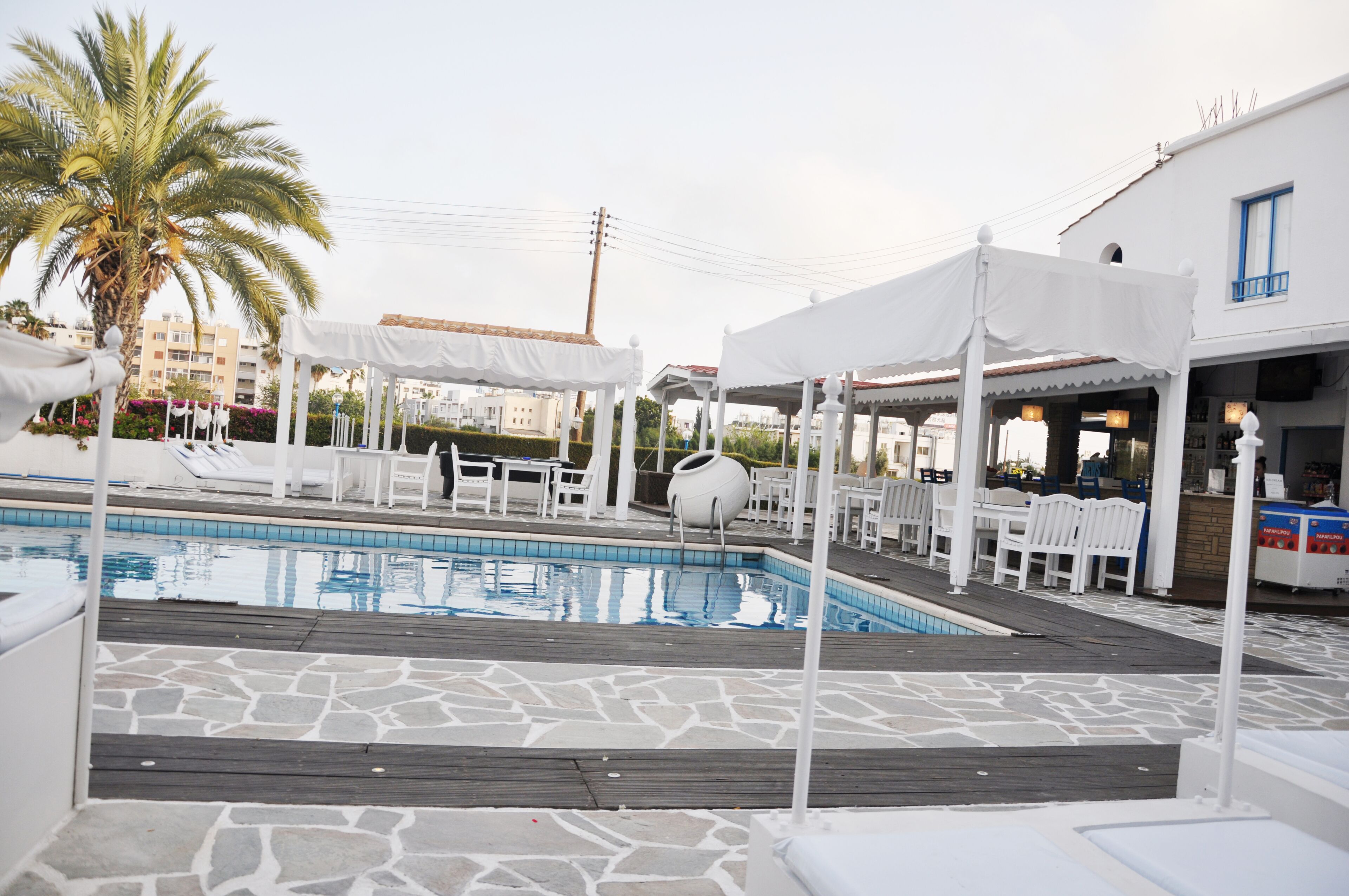 Zona de piscina con toldos blancos, sillas de descanso y una palmera.
