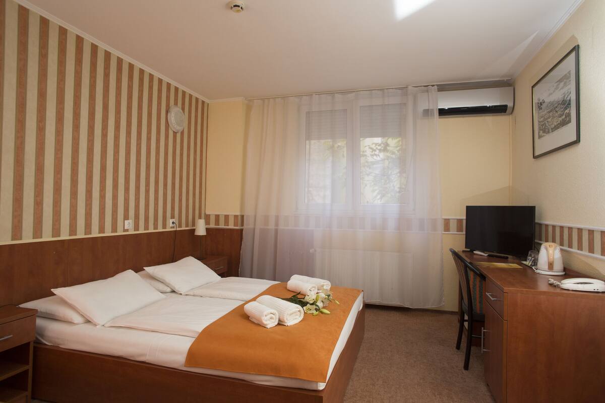 Hotellihuone, jossa on sänky, työpöytä, televisio ja ilmastointilaite.