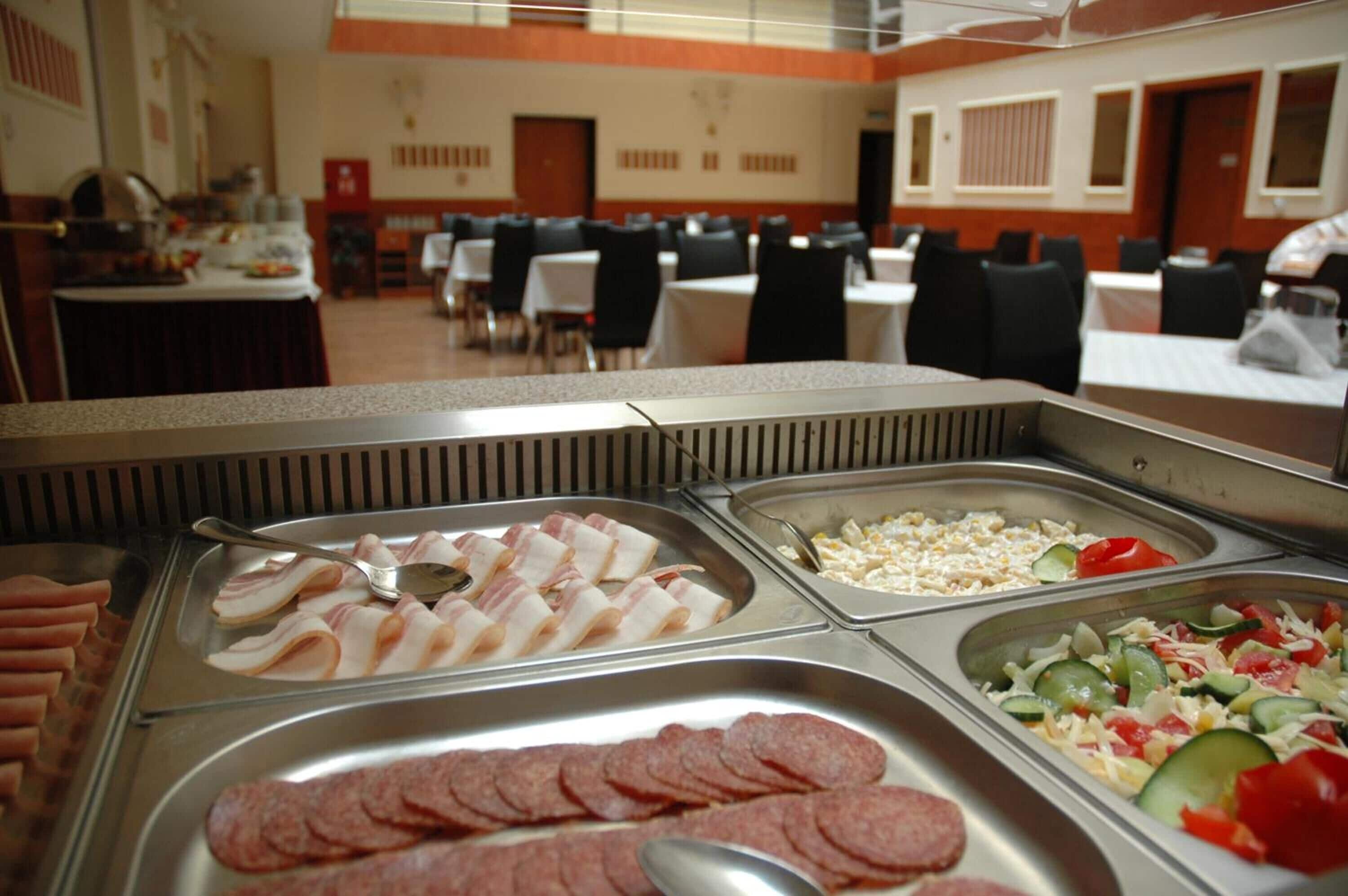 Zona de bufé con diversas opciones de comida, incluyendo tocino, maíz y una ensalada.