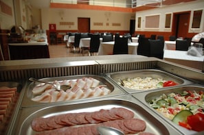 Zona de bufé con diversas opciones de comida, incluyendo tocino, maíz y una ensalada.