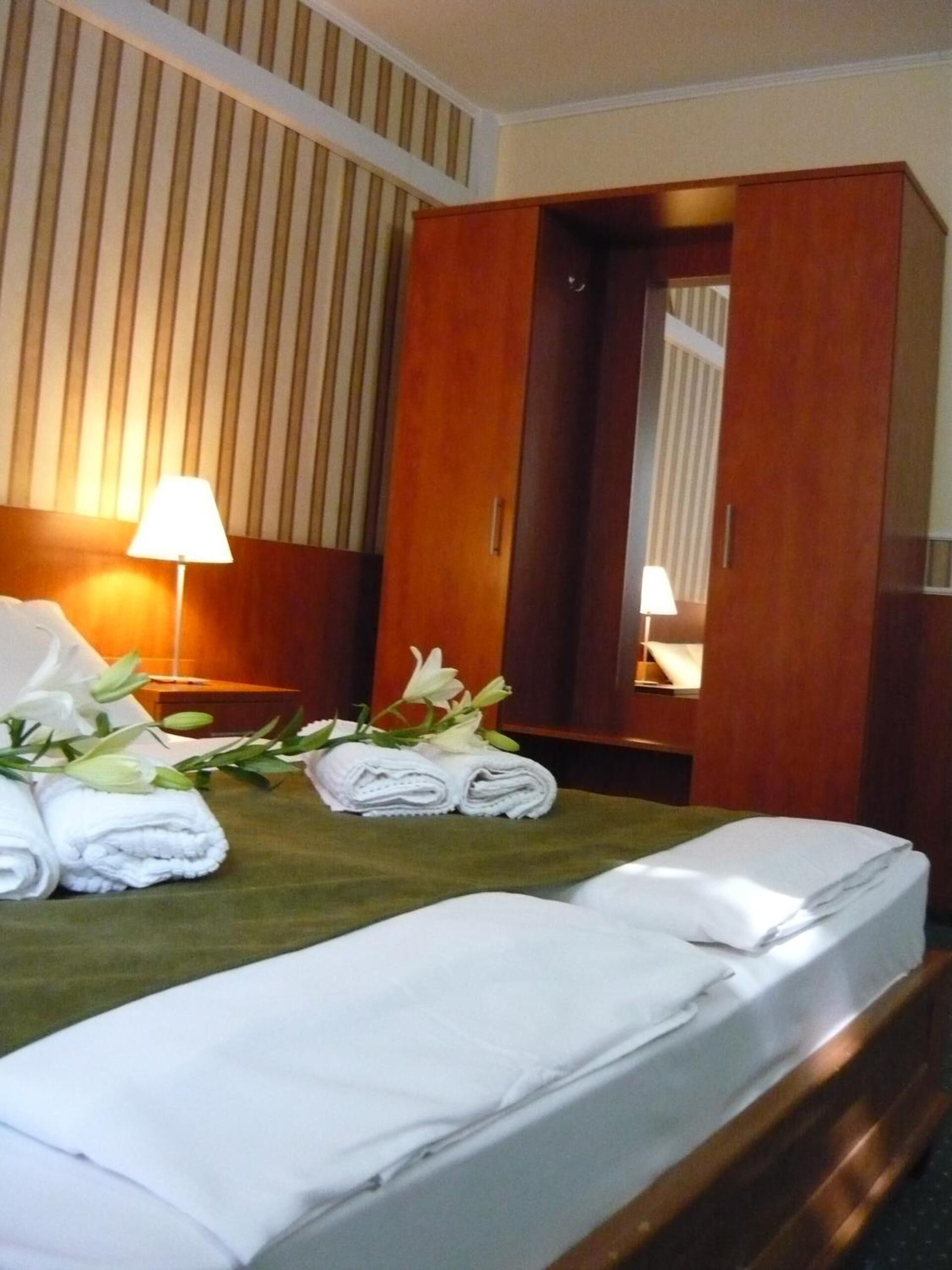 Quarto de hotel com uma cama bem arrumada, um guarda-roupa de madeira e uma luminária em uma mesa de cabeceira.