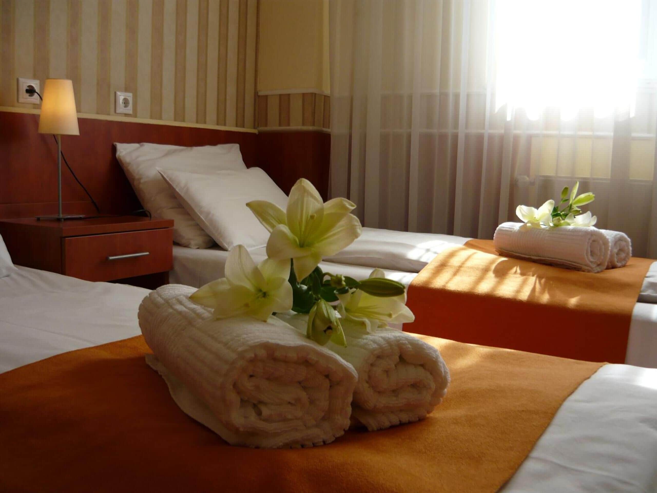 Una habitación de hotel con cama, mesita de noche, lámpara y ventana con cortinas.