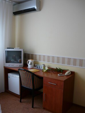 Habitación de hotel compacta con escritorio de madera, refrigerador pequeño, silla, teléfono, hervidor de agua y televisión.