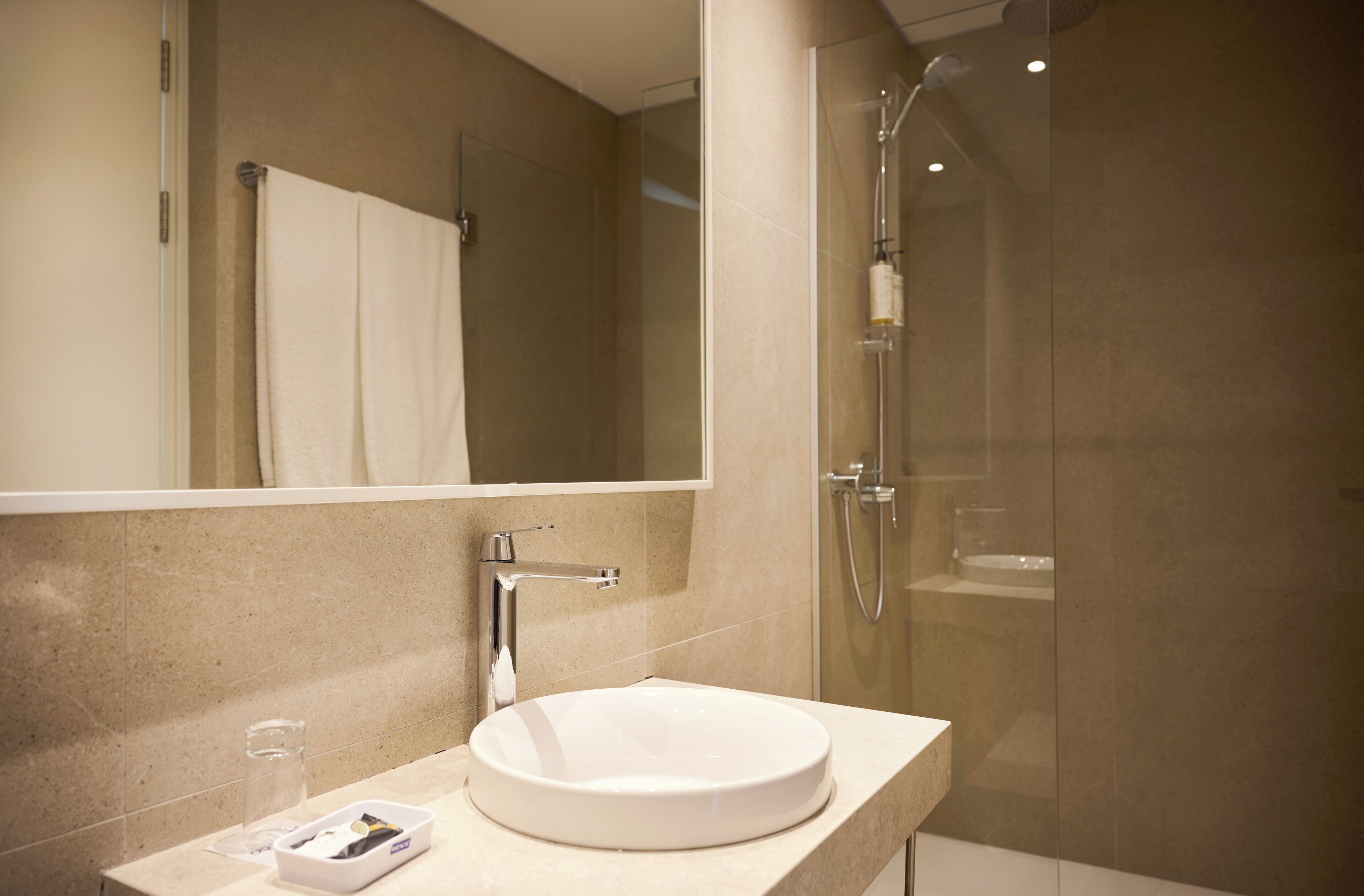 Un baño moderno con un lavamanos redondo, un box de ducha de cristal y un espejo grande.