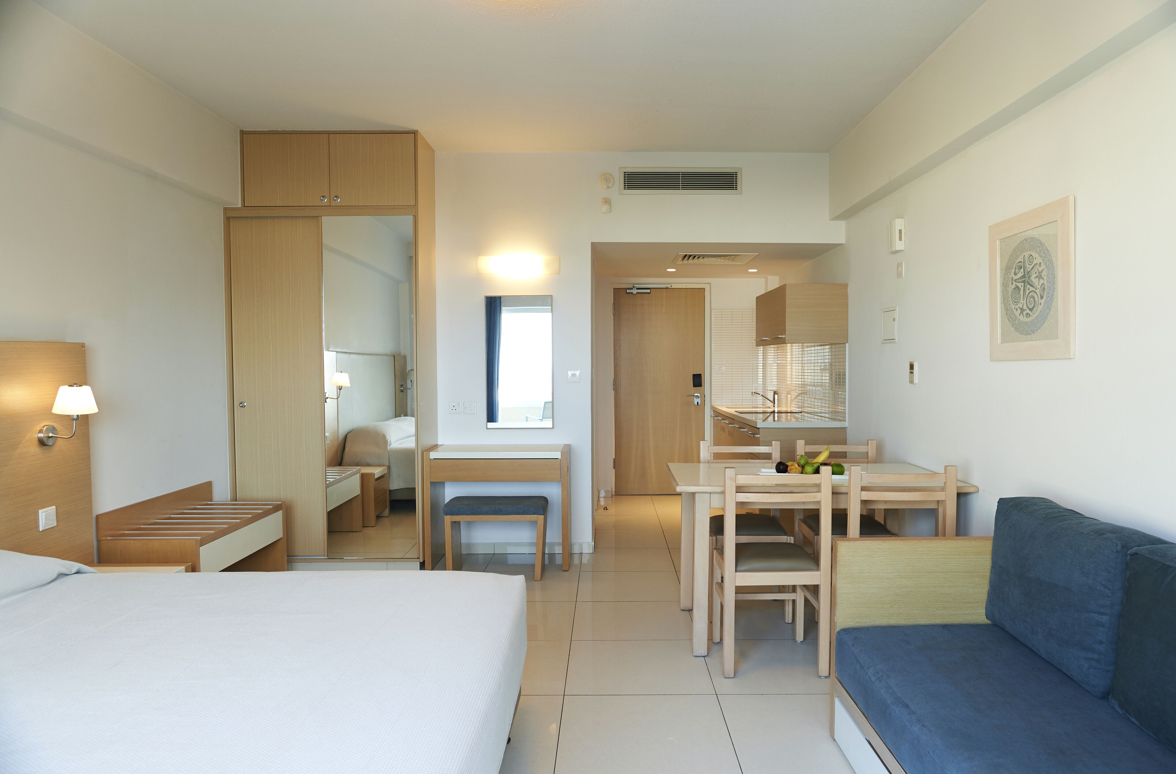 A hotel room with a bed, a desk, a chair, a small table, a bench, and a sofa.