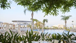 A poolside area with lounge chairs and umbrellas, surrounded by palm trees and a covered seating area. -  Sunrise Oasis Hotel & Waterpark (Paralimni)