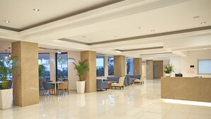 A modern hotel lobby with a reception desk, seating area, and large windows. -  Sunrise Oasis Hotel & Waterpark (Paralimni)