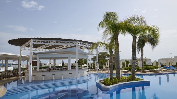 A pool area with a covered bar, lounge chairs, and palm trees. -  Sunrise Oasis Hotel & Waterpark (Paralimni)