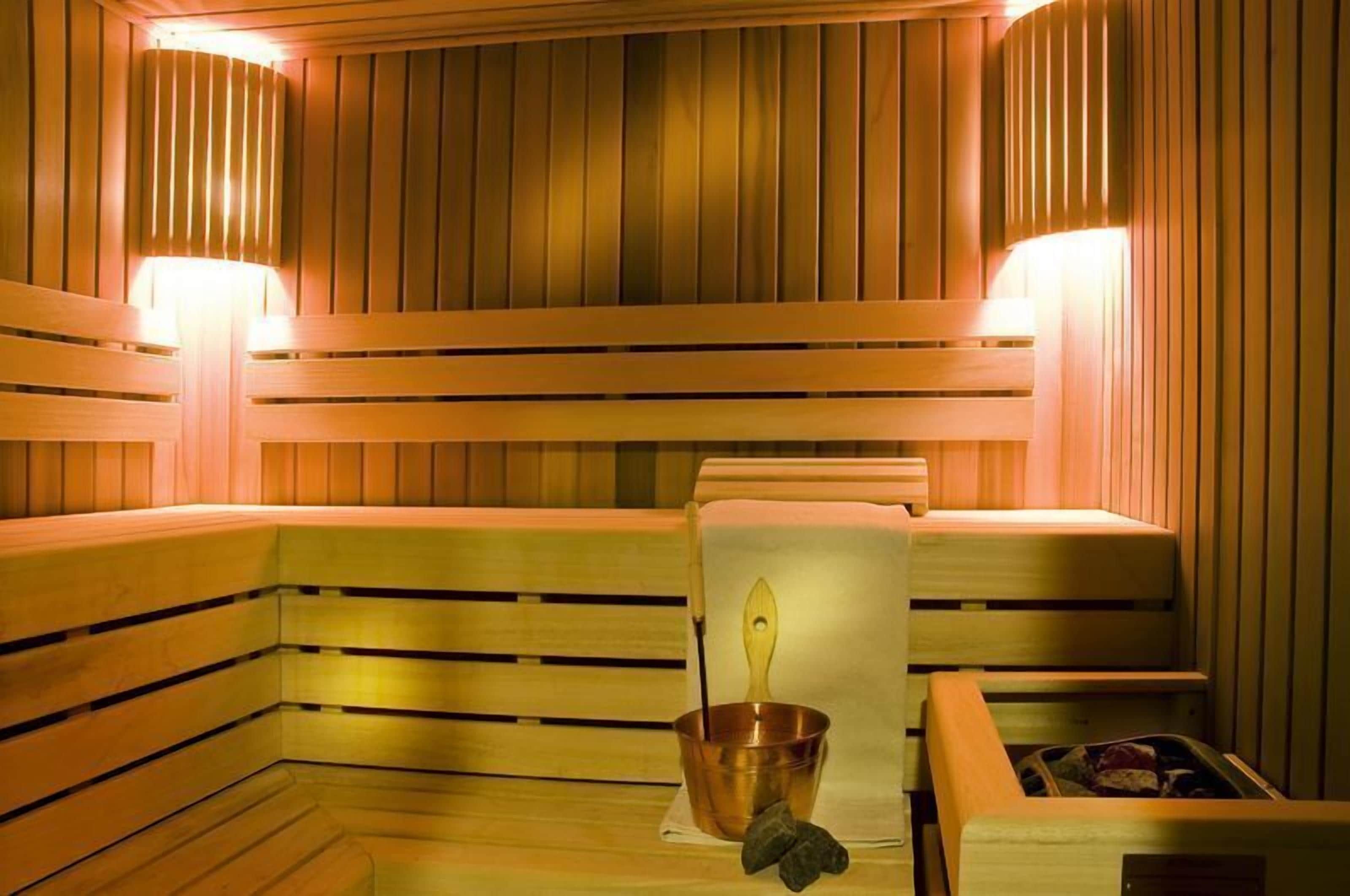 Una sauna con bancos de madera y un cubo de cobre con una cuchara de madera.