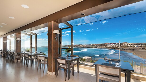 A modern dining area with large windows overlooking a beach and ocean view.