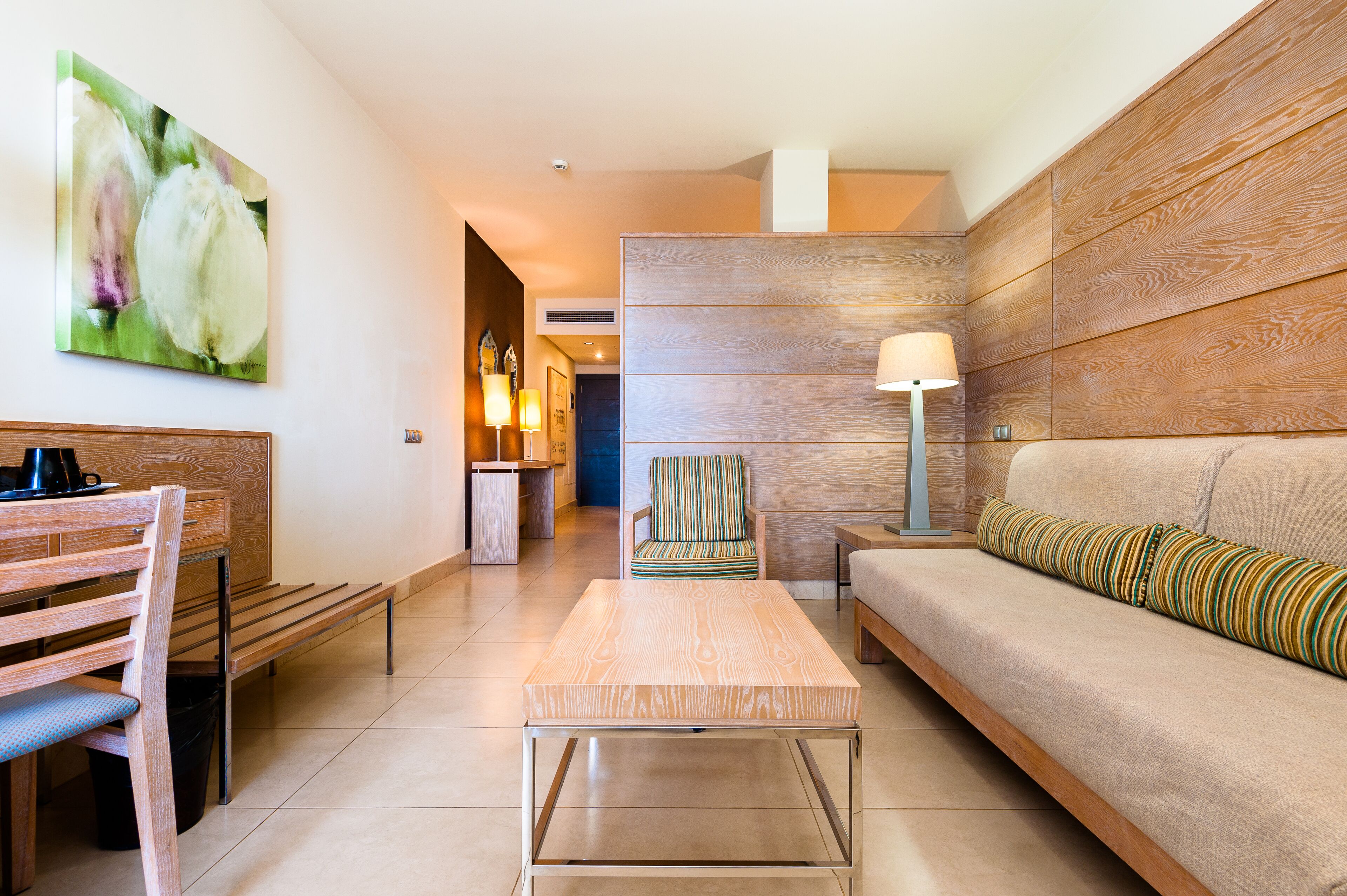 A modern living room with a sofa, a wooden coffee table, a striped armchair, and a painting on the wall.