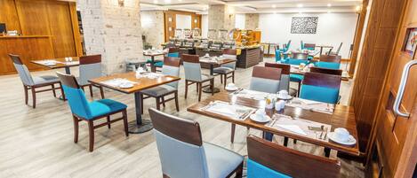 A modern dining area with wooden tables and chairs, a buffet station, and a stone accent wall.