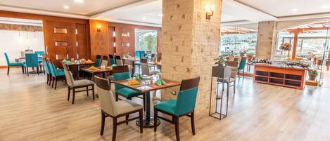 A spacious restaurant with wooden floors, teal chairs, and a central stone pillar.