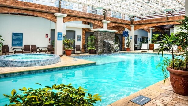 An indoor swimming pool with a glass ceiling, a waterfall feature, and lounge seating. - Sonesta Hotel Loja (Loja)