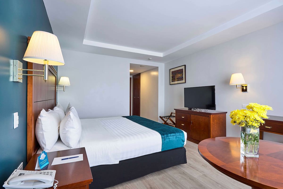 Ein Hotelzimmer mit Bett, Nachttisch, Lampe, Schreibtisch, Stuhl und Fernseher.
