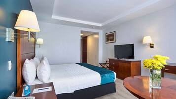 Una habitación de hotel con cama, mesita de noche, lámpara, escritorio, silla y televisor.