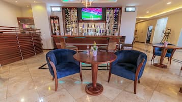 A hotel lobby with a bar area, a television screen, and a seating arrangement.