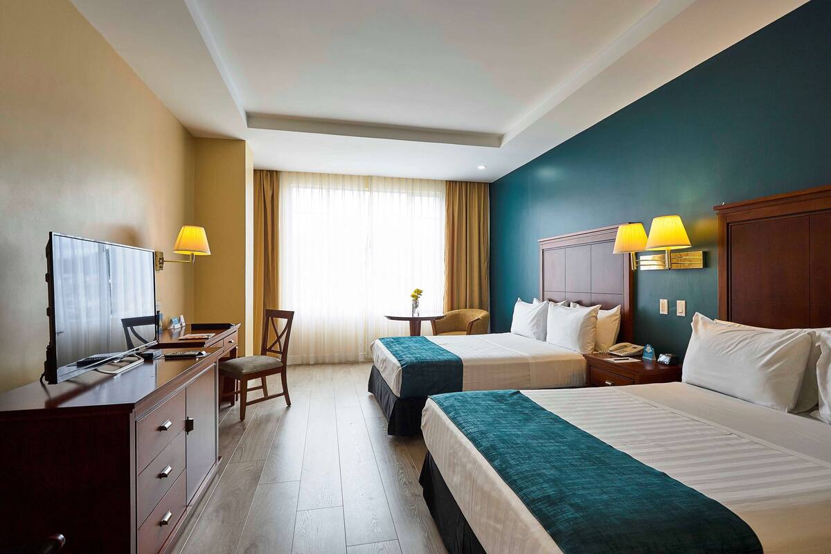Ein Hotelzimmer mit zwei Betten, einem Schreibtisch, einem Fernseher und einem Stuhl.