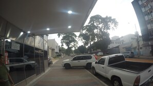 A hotel entrance with a covered walkway, parked vehicles, and a building with a sign.