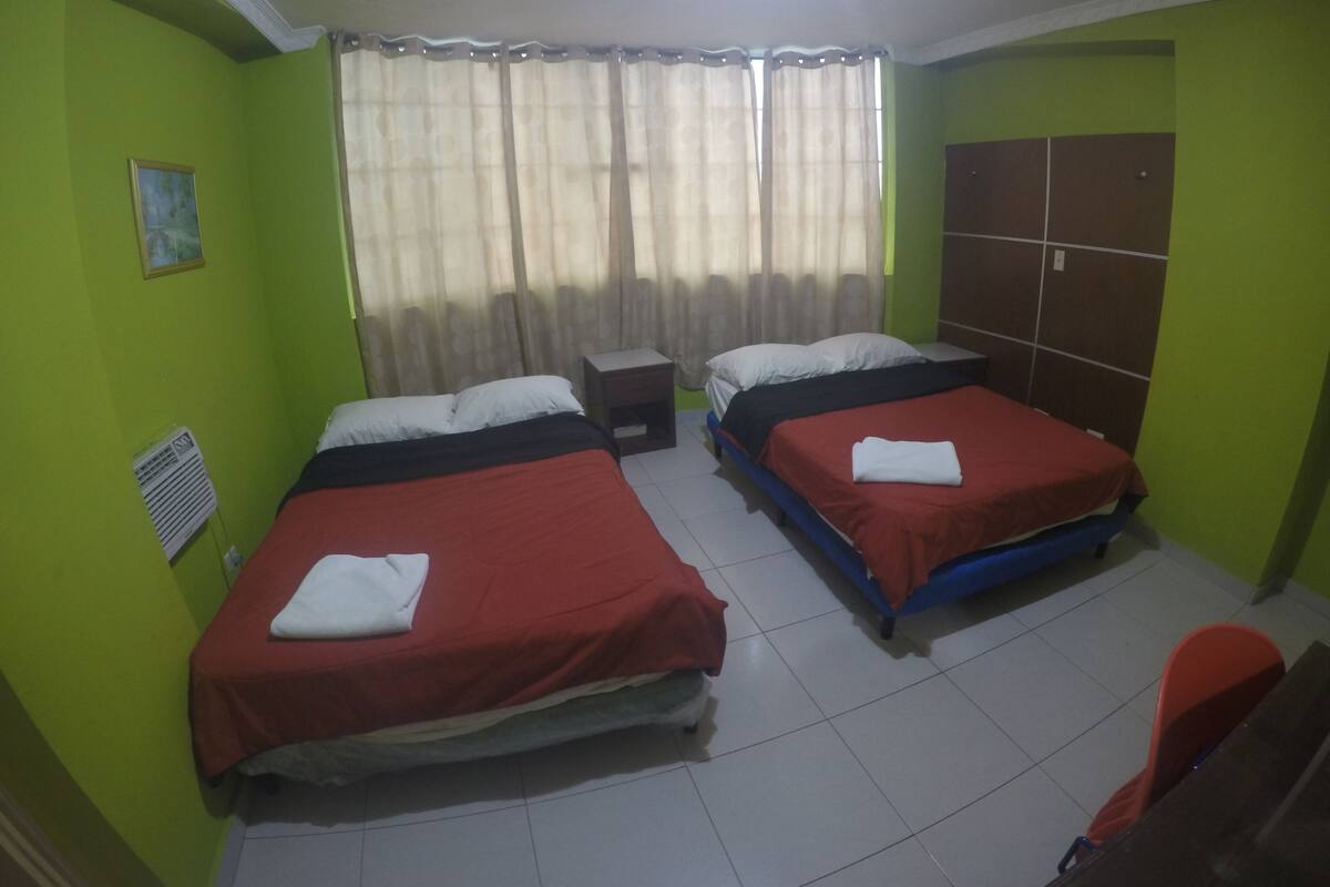 Una habitación con dos camas, una ventana con cortinas, un radiador y un armario.