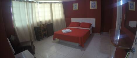 A hotel room with a bed, a desk, a chair, and a small table.