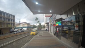 A street view with a sidewalk, a yellow taxi, and storefronts including a neon sign.