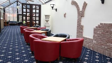 A cafรฉ with red upholstered chairs, a patterned carpet, and a brick wall accent.