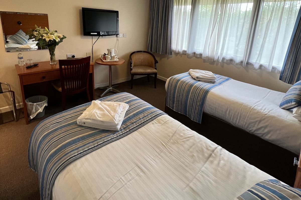 Una habitación de hotel con dos camas, un escritorio con silla, un televisor y una ventana con cortinas.