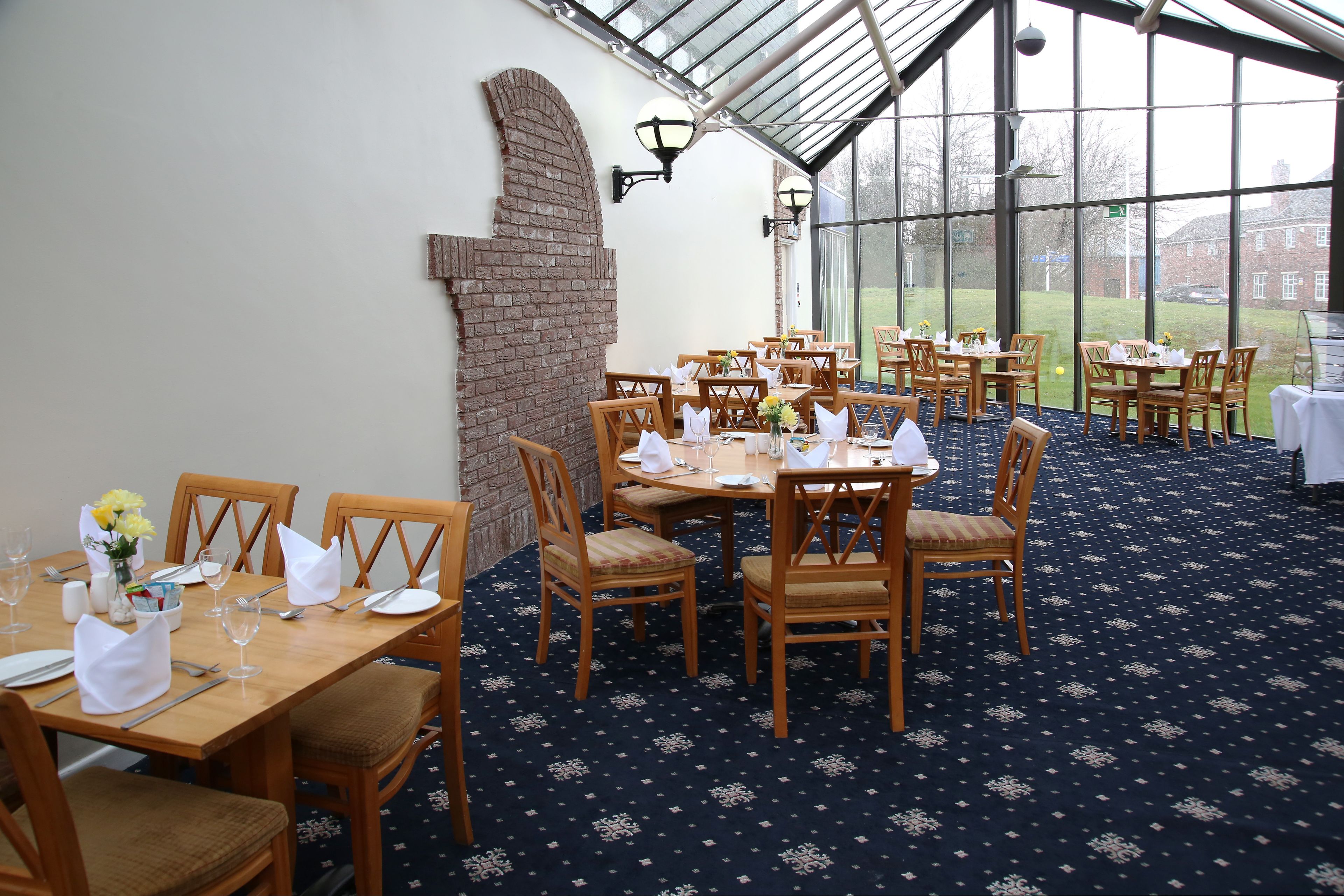 Een restaurant met houten tafels en stoelen, een bakstenen muur en grote ramen.
