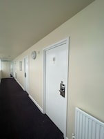 Pasillo de hotel con puertas blancas, cada una con un número y una cerradura.