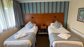 Une chambre d’hôtel avec deux lits, une tête de lit en bois, des rideaux à rayures et un tableau au mur.