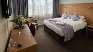 Habitación de hotel con cama, escritorio, silla, televisor y ventana con cortinas.