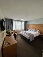 Habitación de hotel con cama, escritorio, silla, televisor y ventana con cortinas.